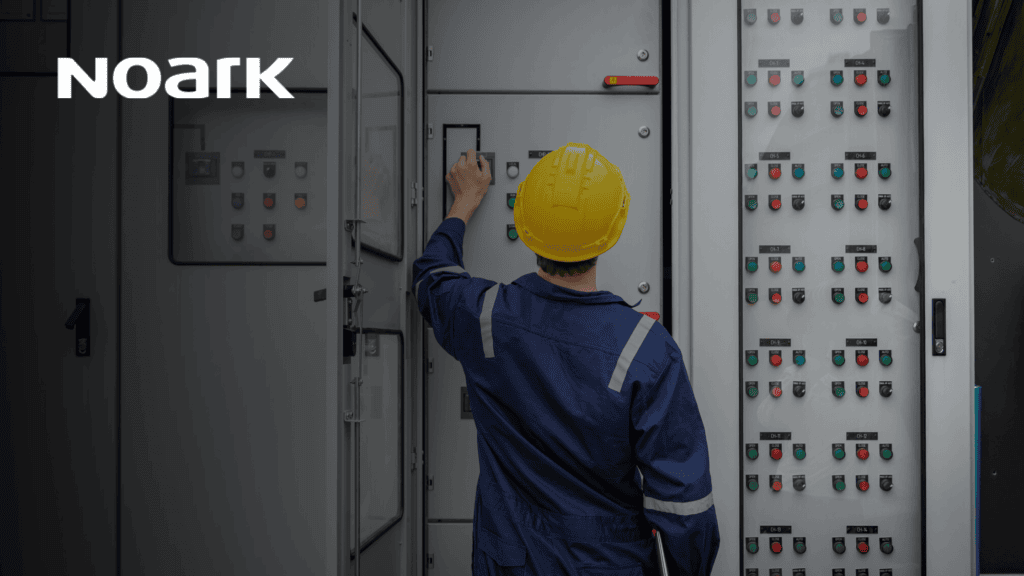 A worker in a blue uniform and yellow helmet skillfully manages a control panel, ensuring seamless operation of relay contact systems in an industrial facility. The "Noark" logo is prominently displayed in the upper left corner, highlighting the brand's dedication to quality and innovation.
