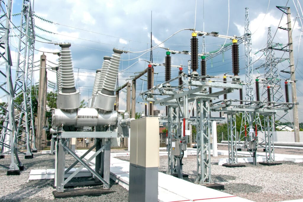 Electrical substation with transformers, circuit breakers, and power lines under a cloudy sky.