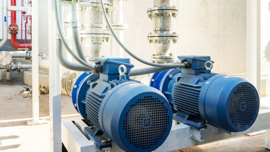 Two large blue industrial pumps with motor units are installed on a metal platform, seamlessly integrated into the factory's water management system, connected by pipes and cables.