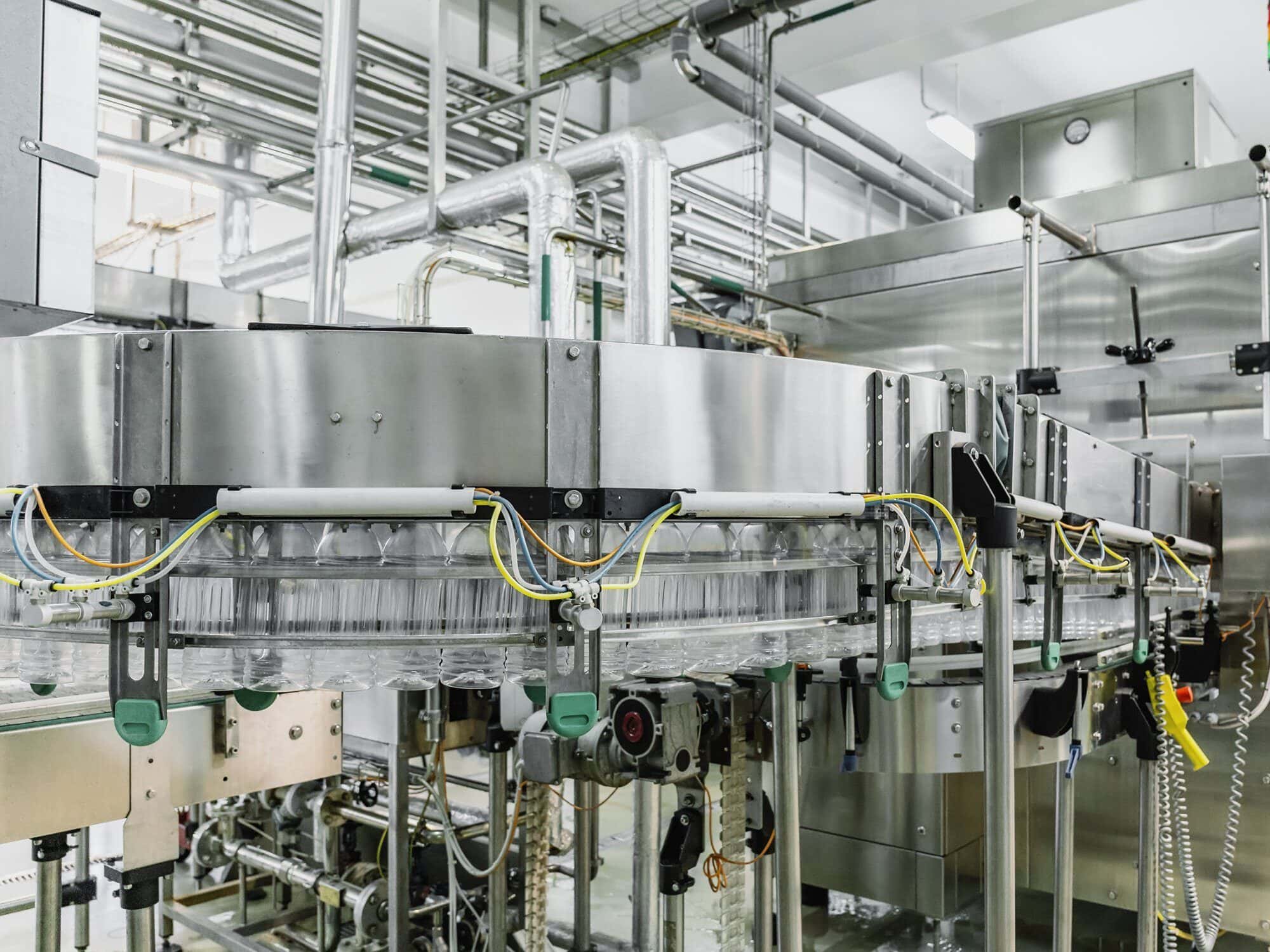 Industrial factory interior with a conveyor belt system and metal pipes, displaying organized machinery for production processes.