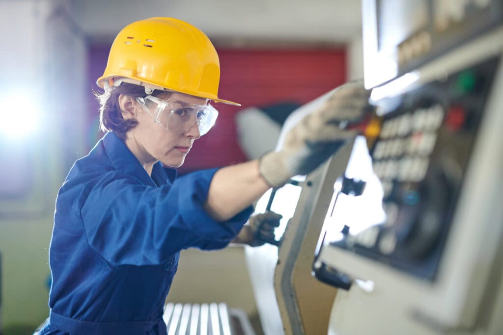 Person in a blue uniform and yellow hard hat operating machinery in an industrial setting.