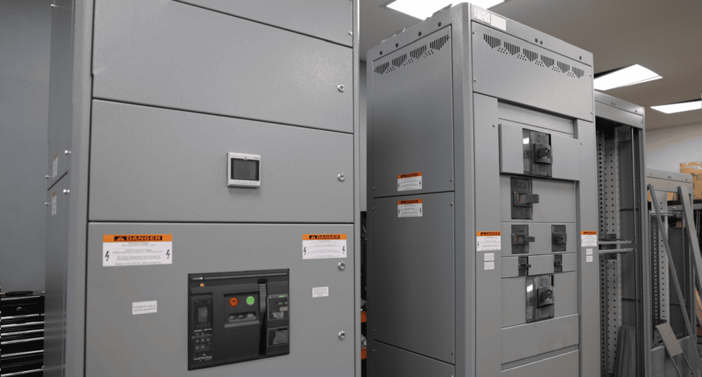 A room filled with large industrial panelboards and warning labels, showcasing an array of switches and control panels beneath fluorescent lighting.